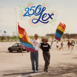 Two people stand in a parking lot with Pride flags, smiling at the camera. Overlaid at the top is colorful text that reads “250 Lex” 