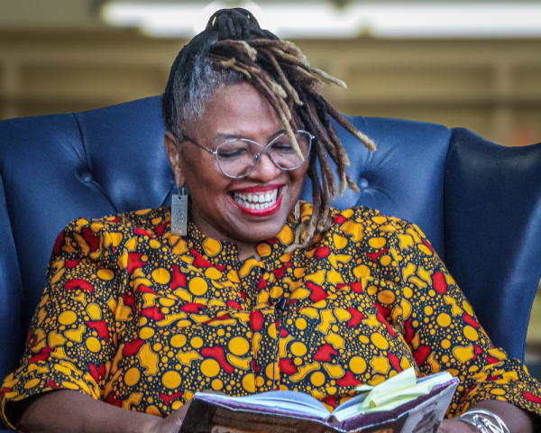 Women sitting in a blue chair and holding a book while smiling and laughing 